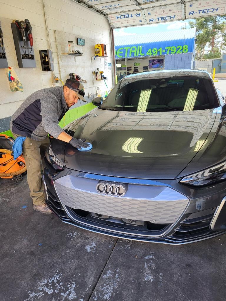 Technician hand-polishing the hood of a gray Audi e-tron GT in the shop bay