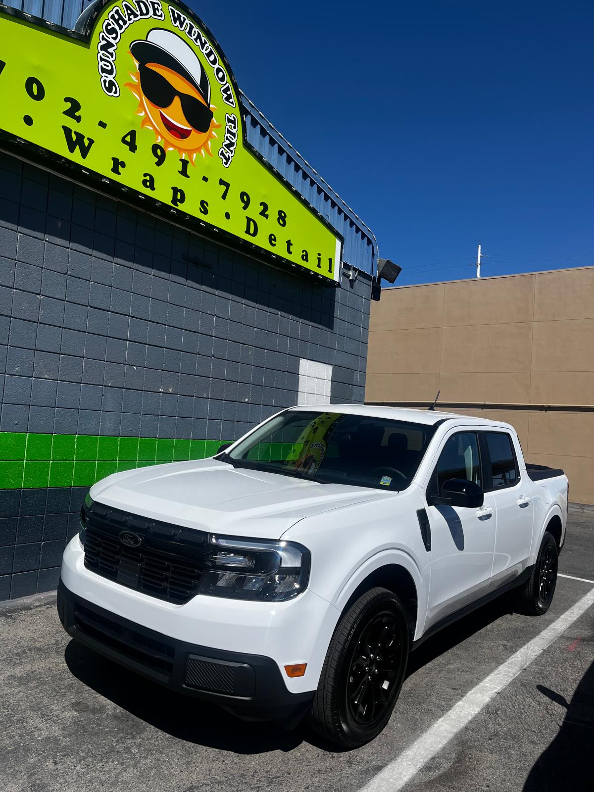 White Ford Maverick parked in front of Sunshade Window Tint shop signage